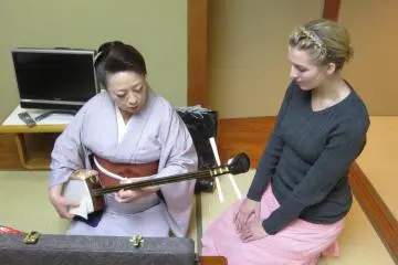 외국인에게 샤미센을 연습시키는 마도카.그녀는 샤미센의 스승이기도 하다.