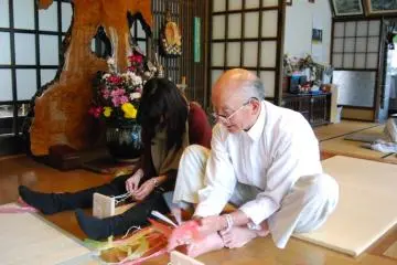 <p>คุณซาซากิสอนการวางเส้นด้ายไปทางขวางก่อนเริ่มถักรองเท้าโซริ</p>